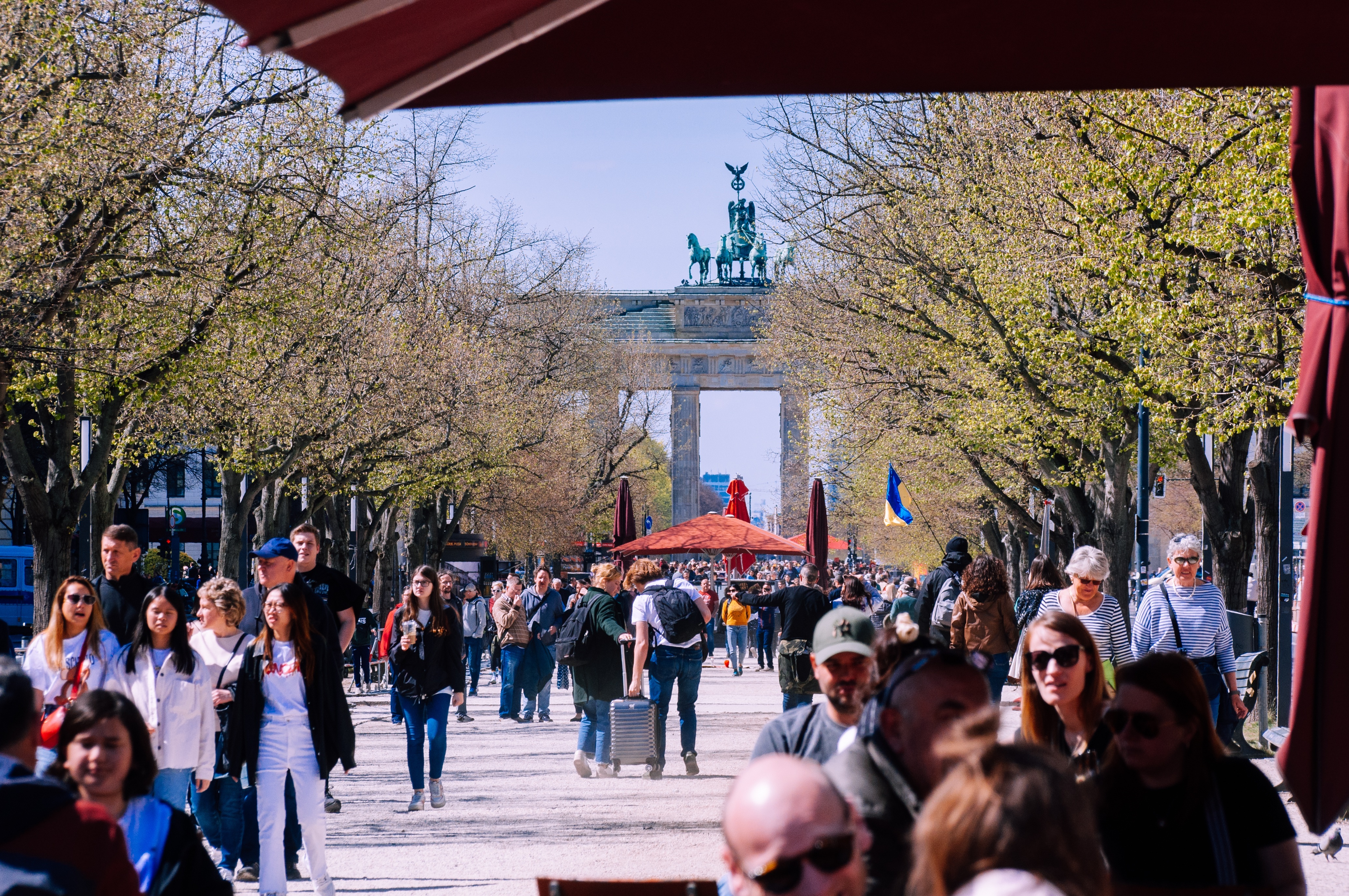 View of the Brandenburg Gate from the street Unter den Linken. Many people are walking on the street.